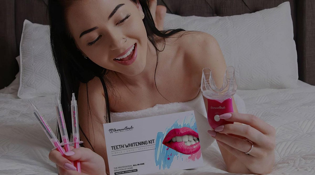 Een vrouw met een tandenbleek set op een bed. Drie spuiten met tandbleekgel en een mondstuk met UV-lamp om de tanden witter te maken.